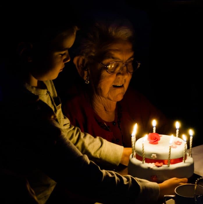 A grandmother lit by birthday candles, a grandchild beside her